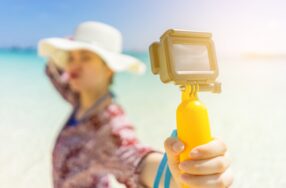 帽子をかぶった女性が海辺でカメラを持って撮影している