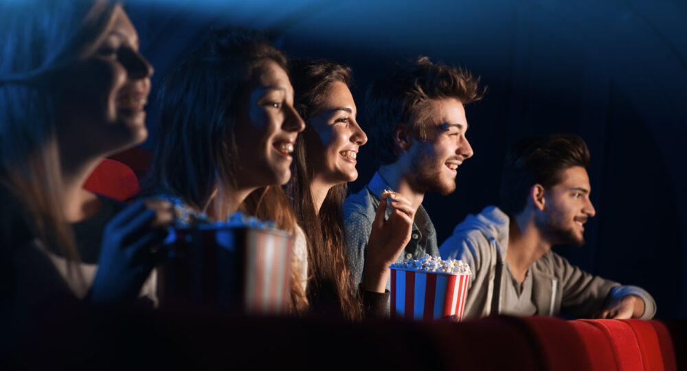 ５人の男女がポップコーンを食べながら映像を見て笑っている