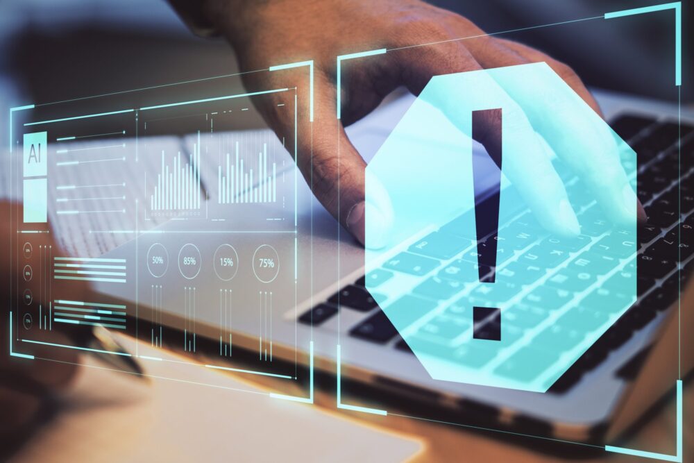 人がパソコンを触っていてモニター画面と青いビックリマークが浮かんでいる