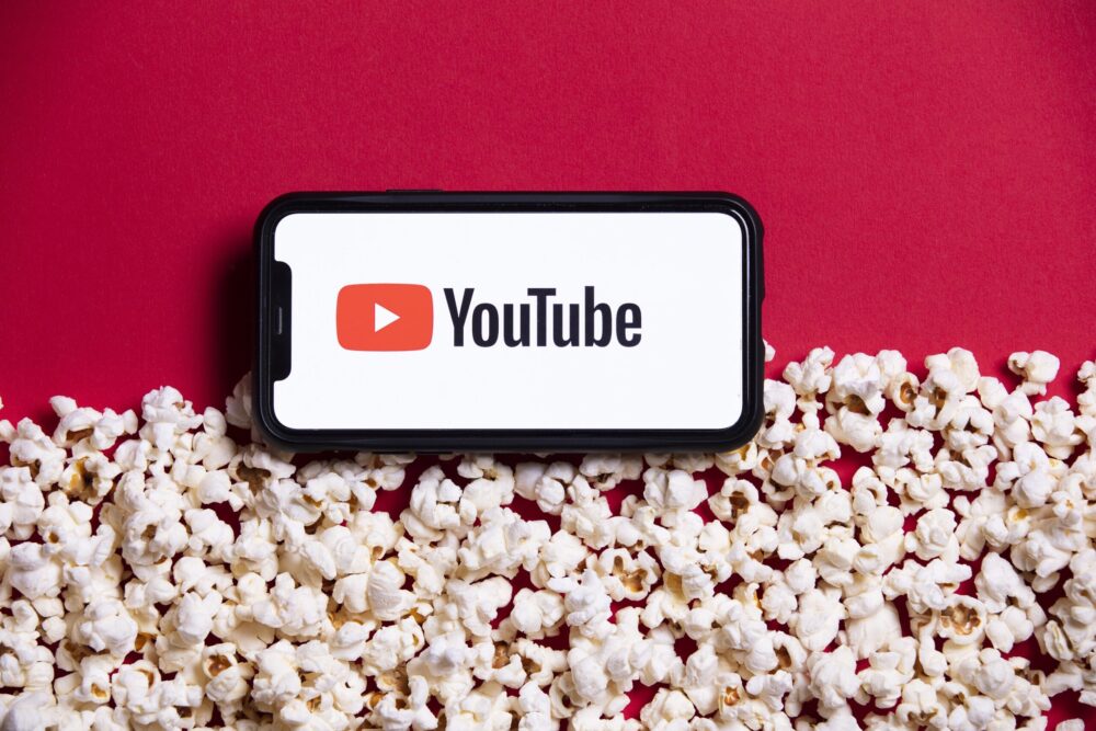 赤い背景にポップコーンとスマホのYou Tubeマークの再生画面が並べられている