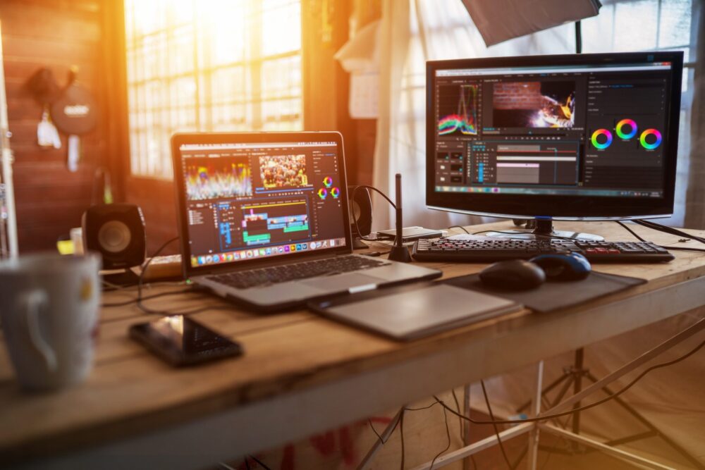 窓から夕暮れが差し込んだ室内のデスクの上に電源の入った２つのPCが並んでいる